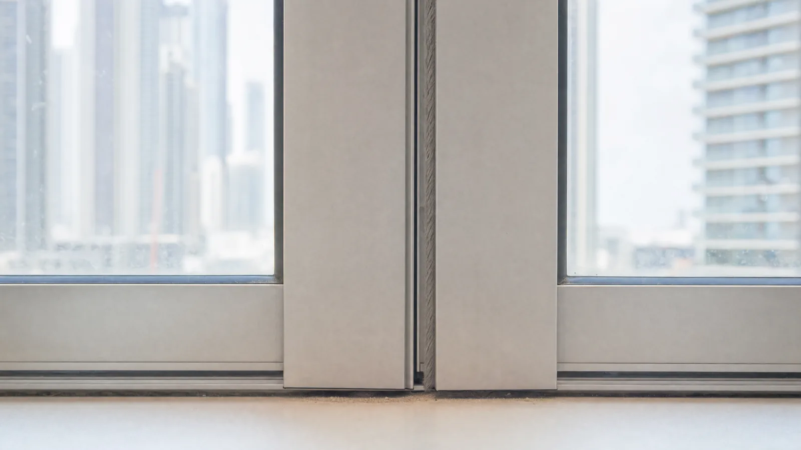 Close-up of the meeting stile where two aluminium sliding door panels overlap in a Dubai apartment, with a worn brush seal visible along the joint