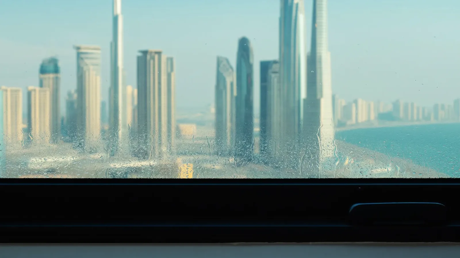 Cloudy haze and trapped water droplets across the lower half of a modern black-framed double glazed window overlooking the Dubai Marina towers.