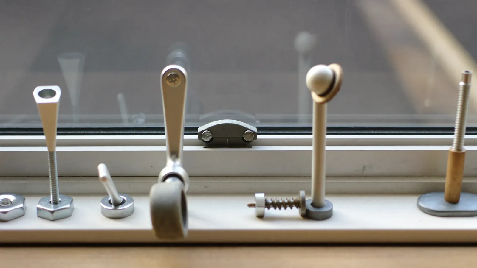 A row of window hardware parts laid out: lock strip, handles, friction stay, roller, keeps and restrictor