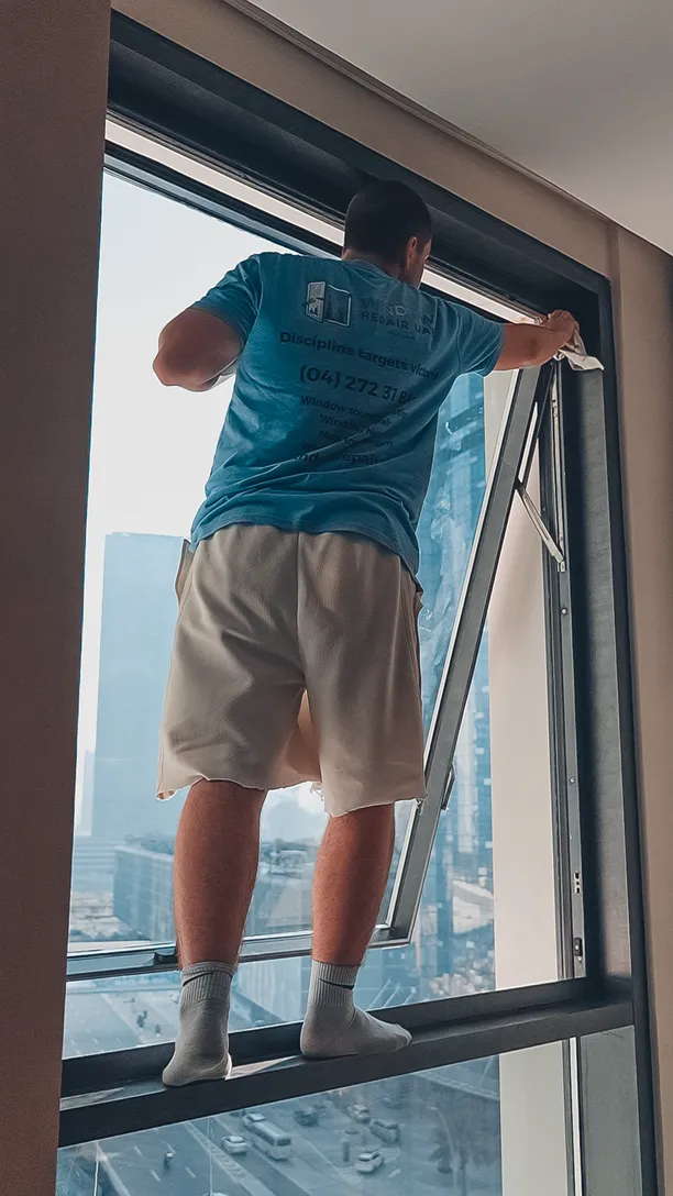 Technician standing on the sill to hold a heavy sash on an upper floor in Dubai