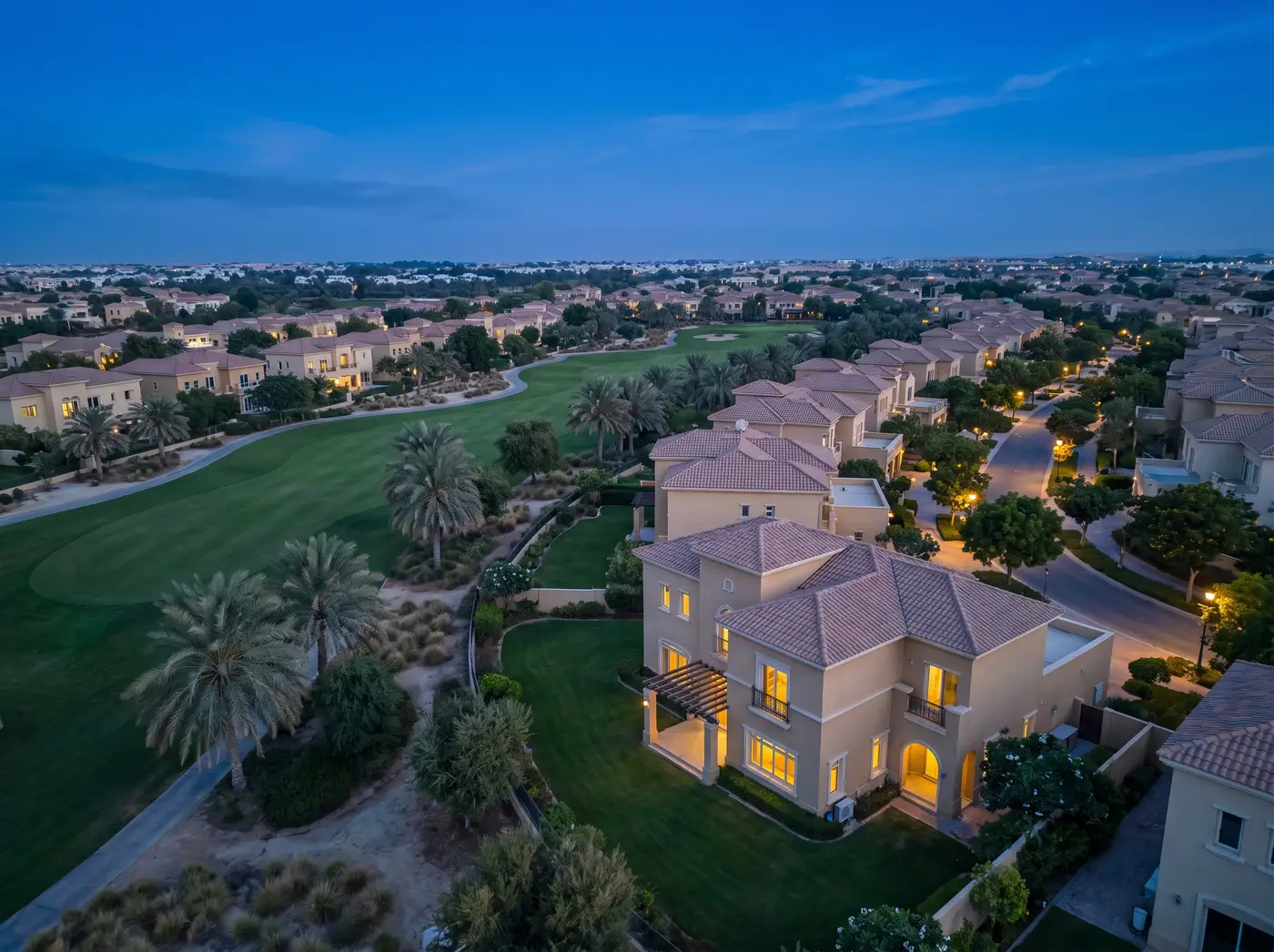 Arabian Ranches villa community at dusk: sand-toned villas, lawns and a golf fairway