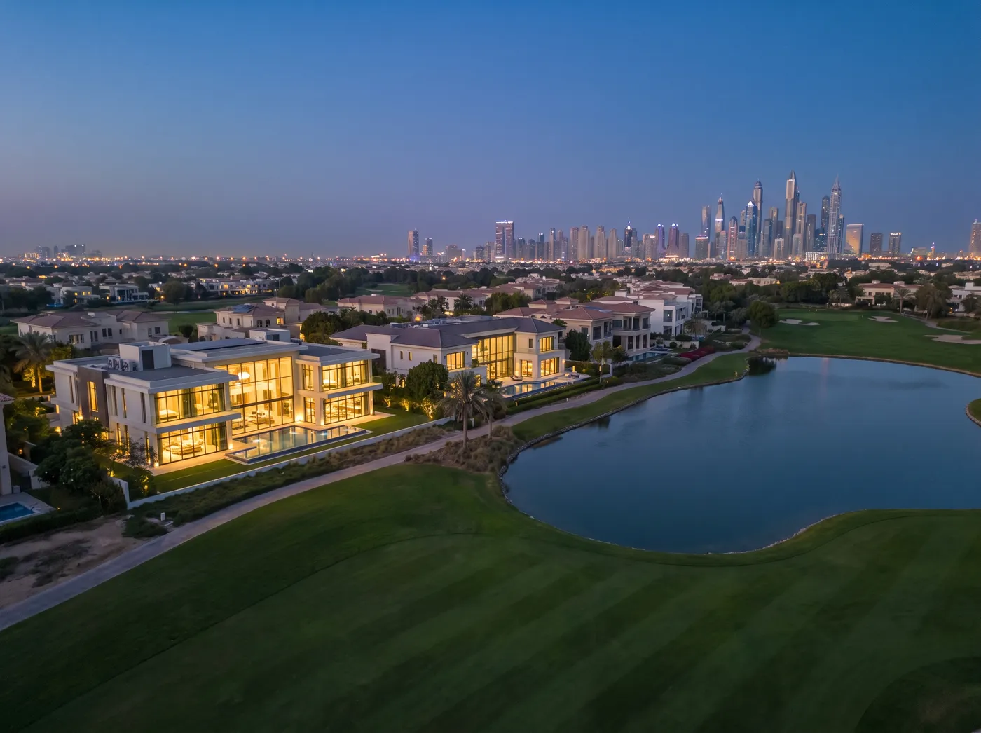 Emirates Hills mansions with large glazing around the golf course lake at dusk