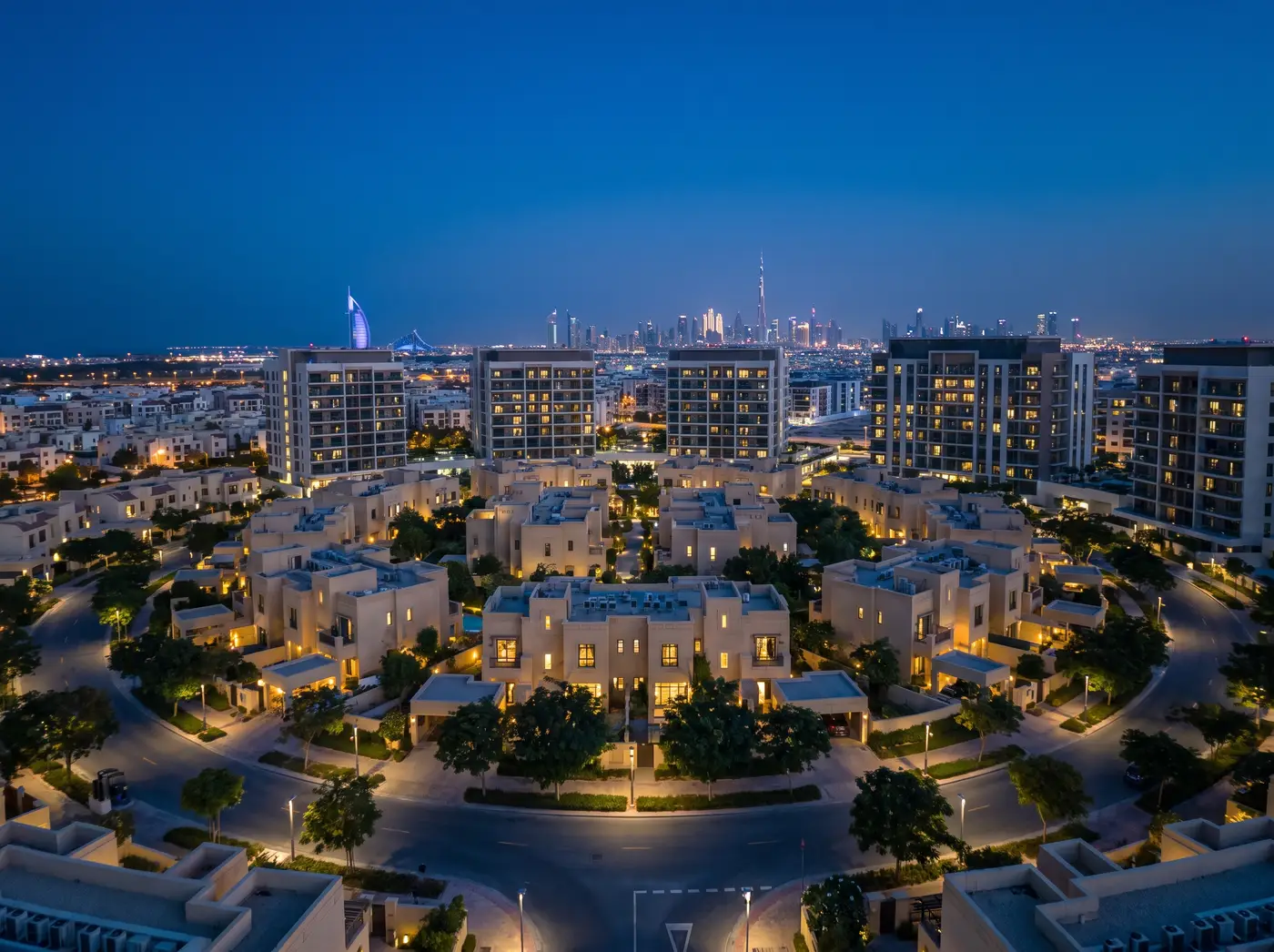 JVC low-rise townhouses and mid-rise blocks at dusk with the Dubai skyline on the horizon