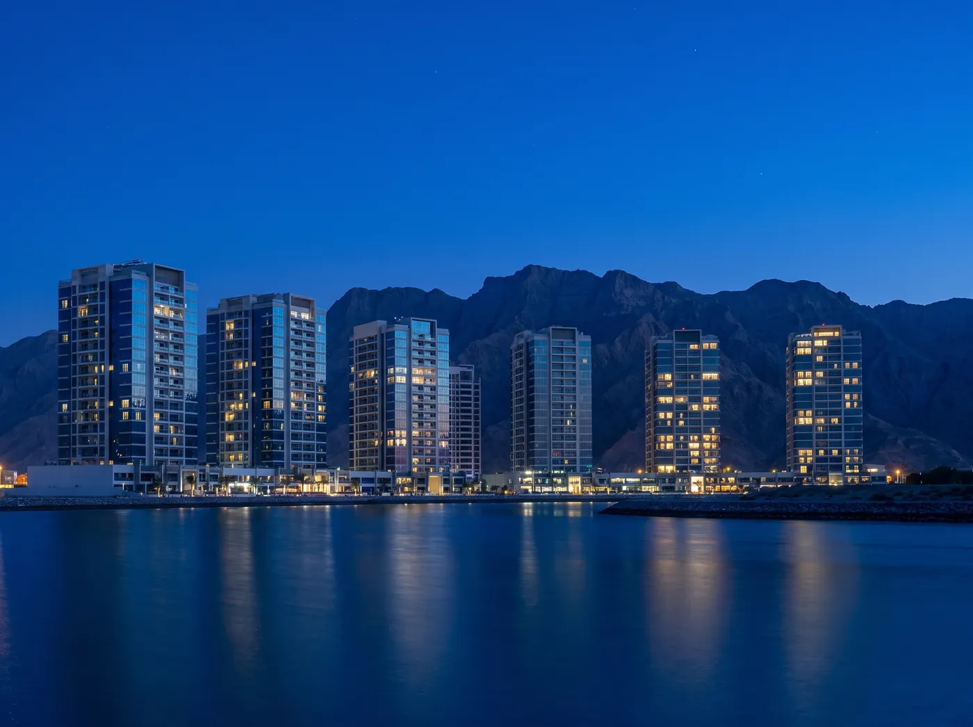 Ras Al Khaimah waterfront towers with the Hajar mountains behind at blue hour