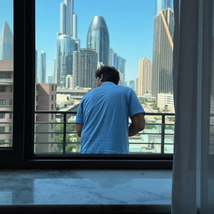 Man at an apartment window looking out over Dubai high-rise towers