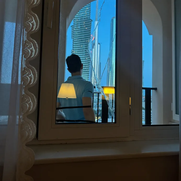 Cracked window pane in a Dubai apartment with a technician inspecting it from the balcony at dusk