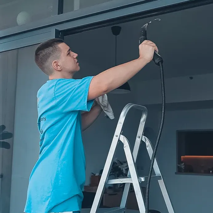 Technician on a stepladder steam-cleaning a window frame