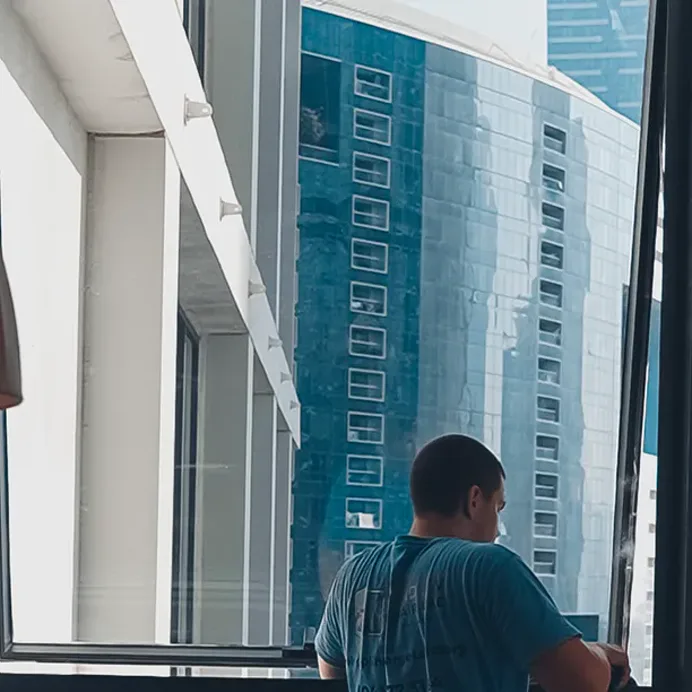 A technician adjusts a casement in a Dubai tower, the city behind the glass
