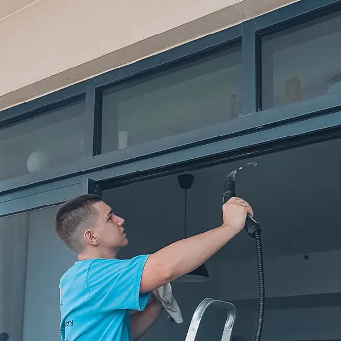 A technician on a step ladder reaching the upper glazing of a room